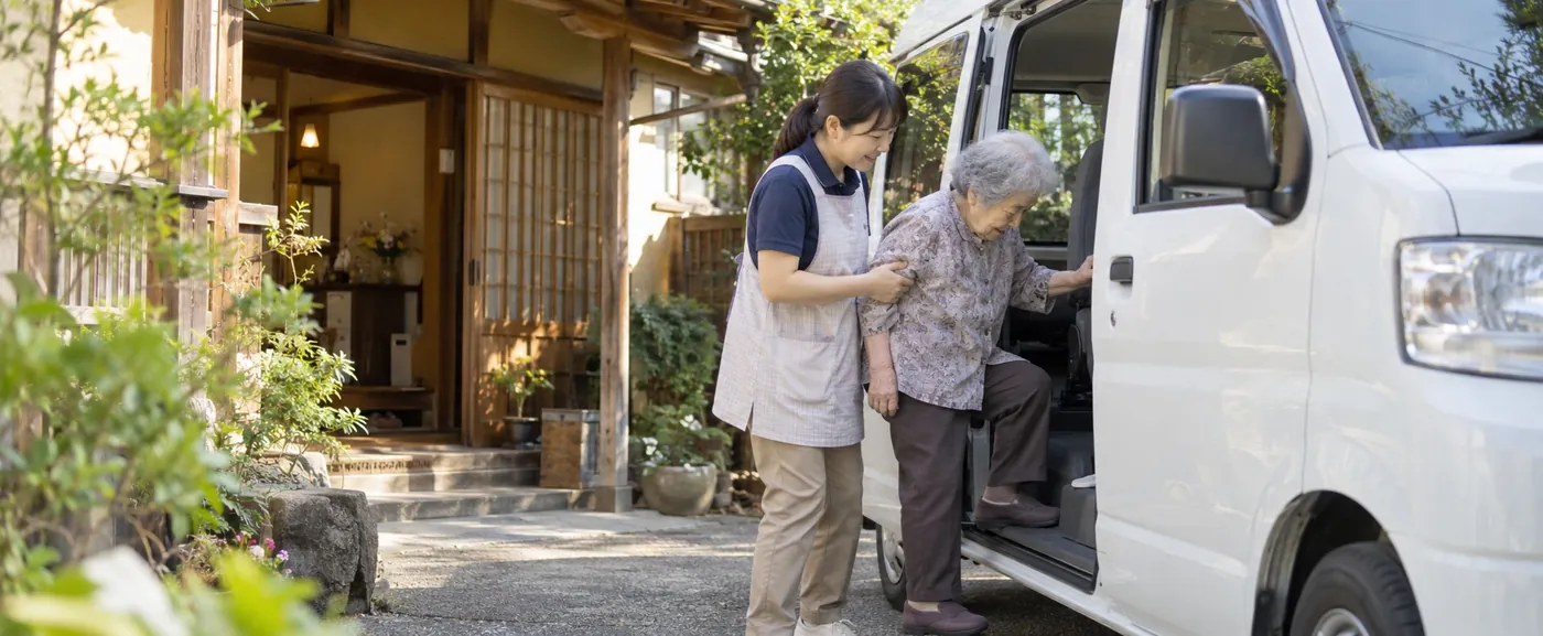 玄関先で利用者の乗り降りを介助するスタッフ